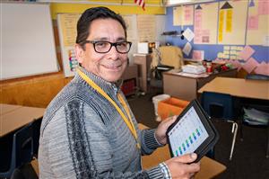 Puente de Hózhó teacher Louis Melo in classroom holding an iPad. 